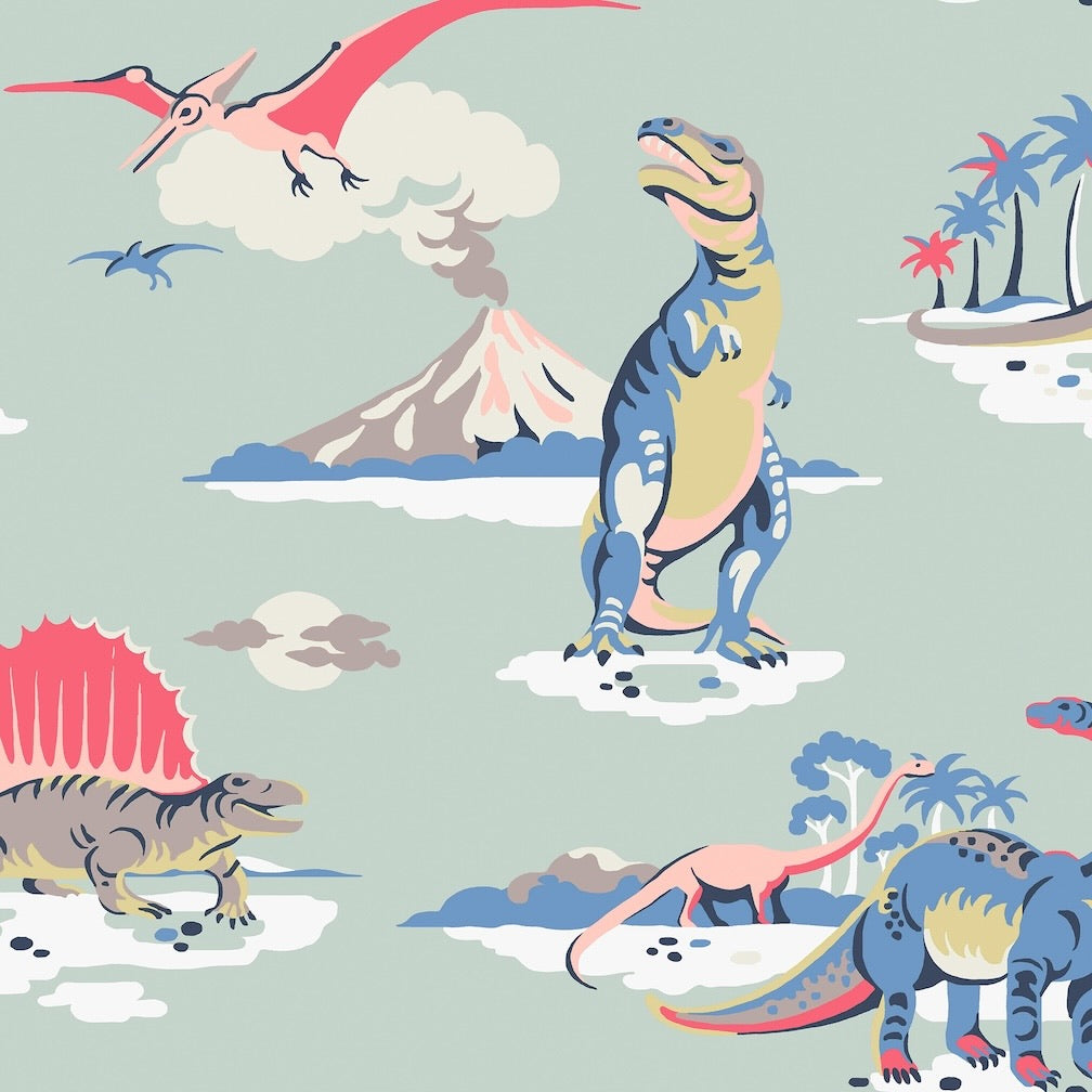 A repeating illustrated dinosaur pattern on a pale sage green background, featuring a blue and yellow standing dinosaur, a pink flying reptile, a volcano, palm trees, and other dinosaurs in muted pastel colors.